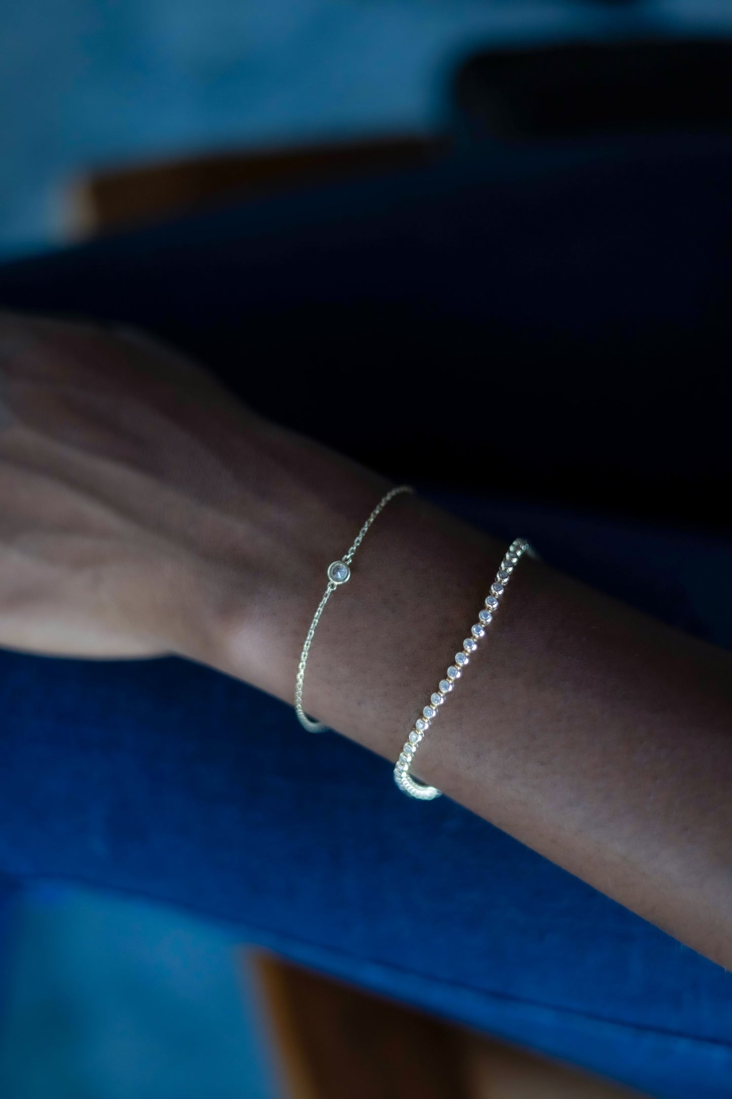 single bezel set diamond bracelet layered with diamond tennis bracelet in 14k solid gold worn on model wrist